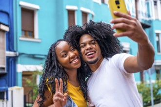 African couple gesturing success taking a selfie in a colorful street