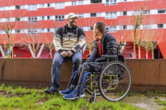 Two male friends, one with a disability, enjoy a conversation outdoors in an urban setting