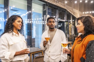 Multi-ethnic coworkers talking while drinking beer in the terrace of a night bar after work