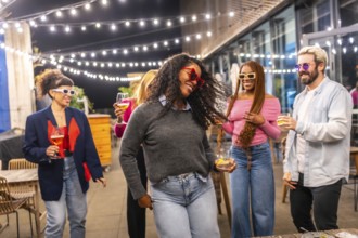 Energetic latina woman dancing with friends at night party in a roof of a bar at city