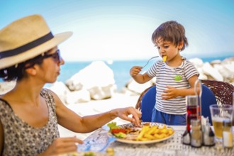 Mother and son are having lunch at a seaside restaurant, enjoying their summer vacation together