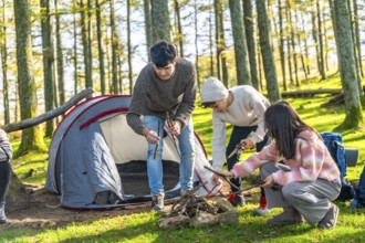 Father, son and daughter making a bonfire in the forest next to camping tent