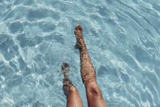 Women's legs in the water of a pool with turquoise water and summer light