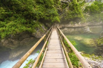 Scenic view of a wooden footbridge spanning a crystal clear emerald river flowing through the
