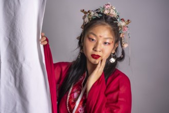 A woman in a red dress with a flower headpiece is posing for a photo. The image has a traditional
