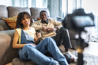 Two young content creators are recording a video blog from their living room, discussing and
