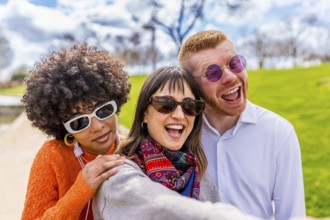 Three cheerful multi ethnic friends are taking a selfie in a park, laughing and enjoying a