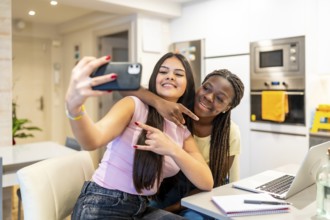 Two happy multi ethnic teenage girls taking a selfie with smartphone while doing homework in a
