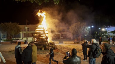 People gather around a burning pile of wood at night, some take photos, Easter fire Psinthos, Holy