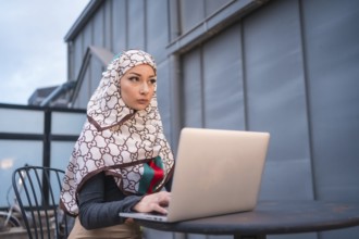 Arab girl with a white veil at the computer on the terrace of a coffe shop, contrabass with the