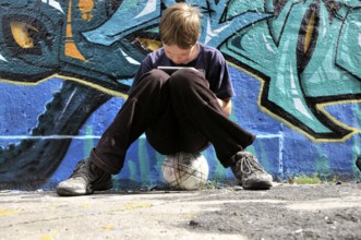 Ten-year-old boy playing with his Nintendo in front of a graffiti wall, football pitch, Germany,