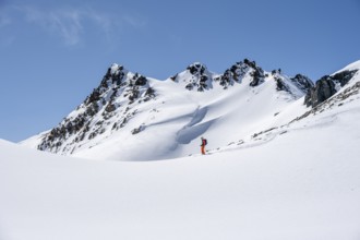 Ski tourer on the descent, minimalist winter landscape, white snow and dark mountains on the