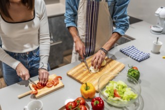 Young couple slicing fresh vegetables on wooden cutting boards, preparing a healthy salad together