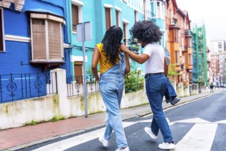 Rear view of two african american young friends walking along a colorful street
