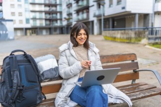 Caucasian smiling woman using laptop sitting on a park in a city square during a cold day