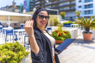 Friendly businesswoman inviting to follow her while using digital tablet on a luxury terrace