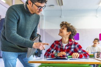 Elementary school teacher engaging with a smiling student while explaining a lesson at their desk