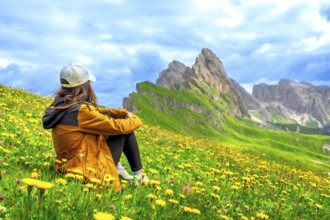 Tourist admiring seceda peaks in the italian dolomites, surrounded by yellow flowers in a sunny