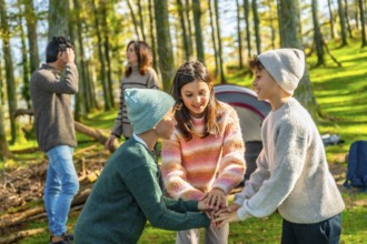 Two caucasian brothers and sister stacking hands playing in the forest enjoying camping with family