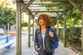 Young latin beauty woman wearing leather jacket walking in the city holding phone