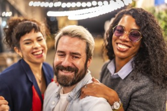 Happy diverse multi-ethnic young friends taking selfie at night party outdoors in a terrace bar