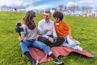 Three content creators are recording an interview for their video podcast in a park, using a