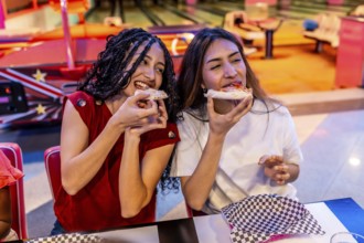 Two joyful young women sharing delicious pizza while enjoying a fun filled day at the bowling