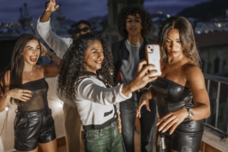 Multi-ethnic elegant friends taking selfie while partying on rooftop at night
