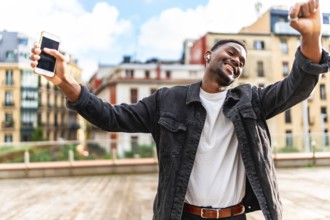 African man dancing happy while listening to music using mobile phone and wireless earbuds in the