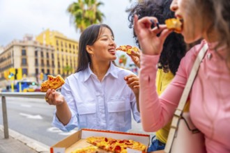 Three multicultural female friends sharing and eating pizza sitting outside