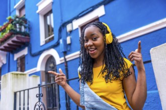 African woman singing while listening to music with headphones standing in a street with blue