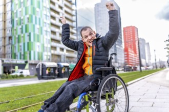 Happy disabled man celebrating in a wheelchair near modern buildings, enjoying his freedom and
