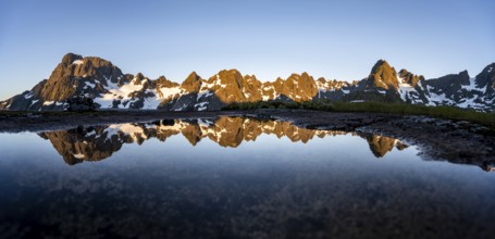 Rocky mountain peaks reflected in a small pond, mountain landscape with alpenglow at sunrise, at