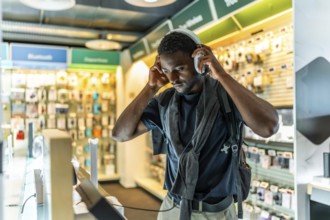 Young african man checking new headphones in electronics store standing alone