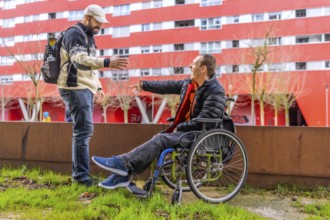 Two male friends meeting in the city, one of them using a wheelchair, greeting each other happily