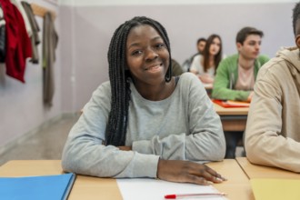 Young black female student is smiling while sitting at her desk in a classroom during a lesson with