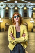 Confident woman in elegant casual clothes and sunglasses standing with arms crossed looking at