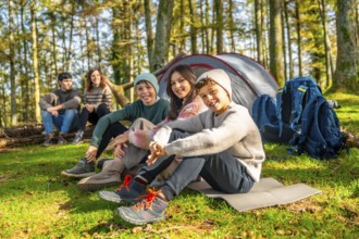 Three kids sitting next to their parents in the forest enjoying together a camping weekend