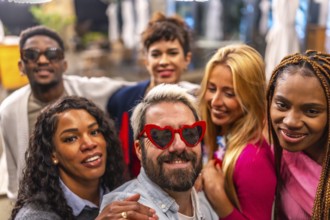 Man with heat shape sunglasses taking selfie with friends outdoors during night in the terrace of a