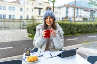 Happy beauty woman enjoying warm tea working with tablet in an outdoor sidewalk cafeteria