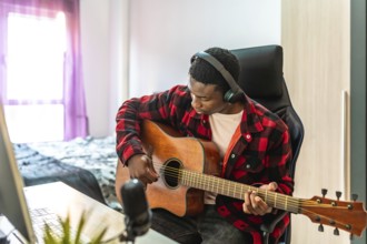 Young man playing acoustic guitar and recording music using a computer and microphone at home