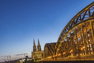Cologne Cathedral, illuminated in the evening. Hohenzollern Bridge, railway bridge over the Rhine.