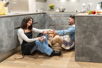 Two chefs are sitting on the floor of their modern kitchen, enjoying a coffee break and chatting