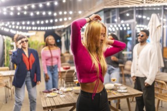 Blonde sensual woman dancing with friends at night party at the terrace of a bar decorated with