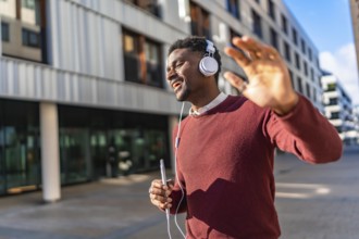 Energetic african young man listening to music and dancing while walking along a city street
