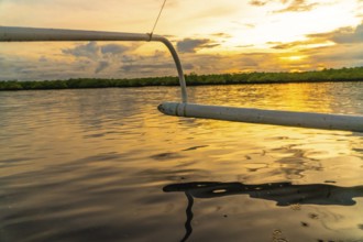 Outrigger of a banca boat sailing on calm water during a golden sunset in siargao island,