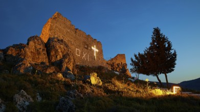 Castle ruins at night with illuminated cross and tree, quiet and historical atmosphere,