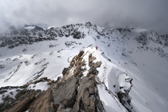 Mountaineer descending the narrow ridge of Piz Laviner, view of mountain panorama in wintry