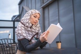 Arab girl with white veil at the computer on the terrace of a coffe shop, having a lot of fun