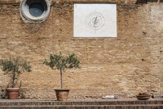 Brick wall with a sundial and two olive trees in a pot on a Mediterranean site, Tuscany, Italy,